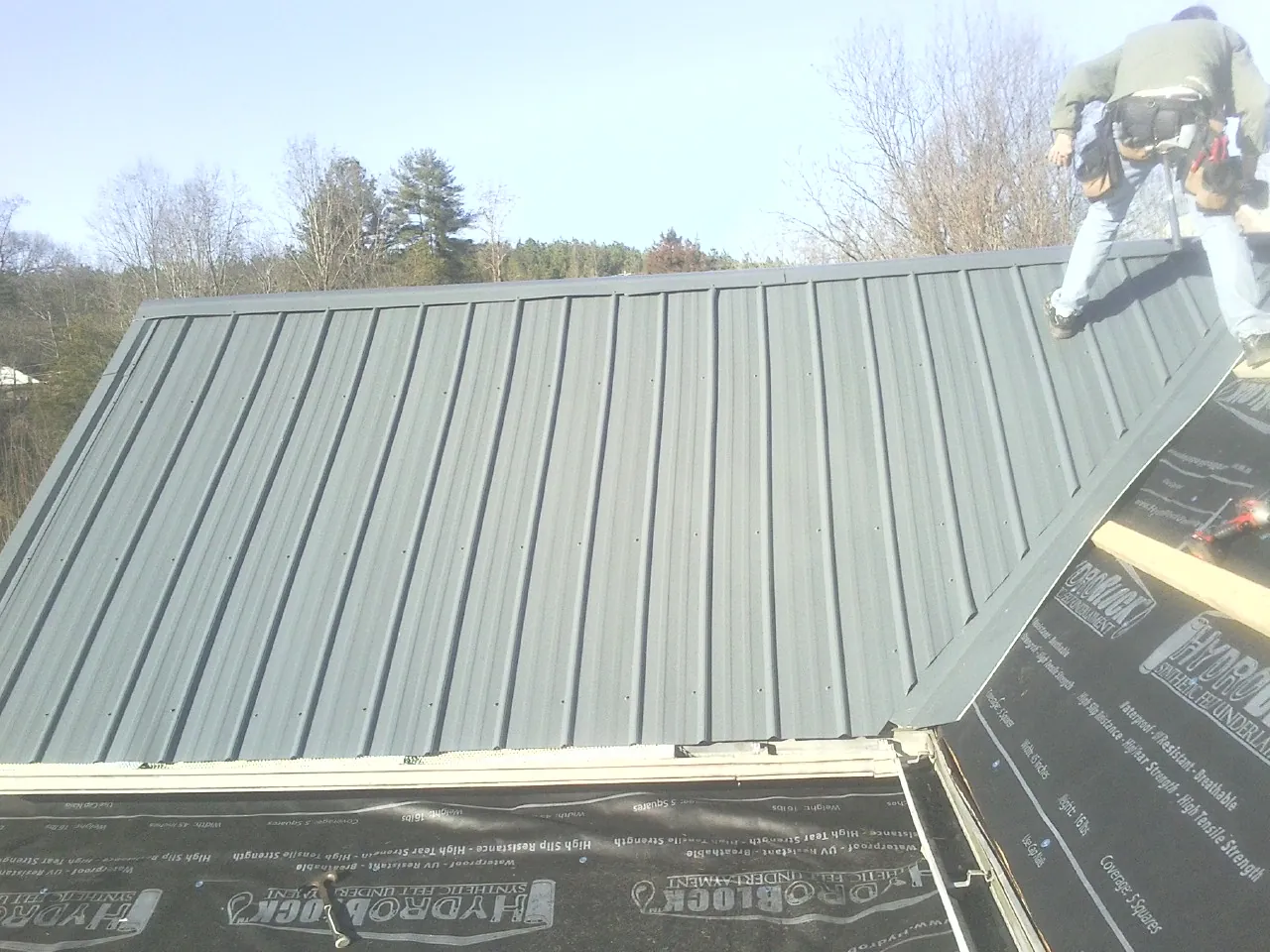 Crew installing dark green standing seam panels over synthetic underlayment in San Angelo