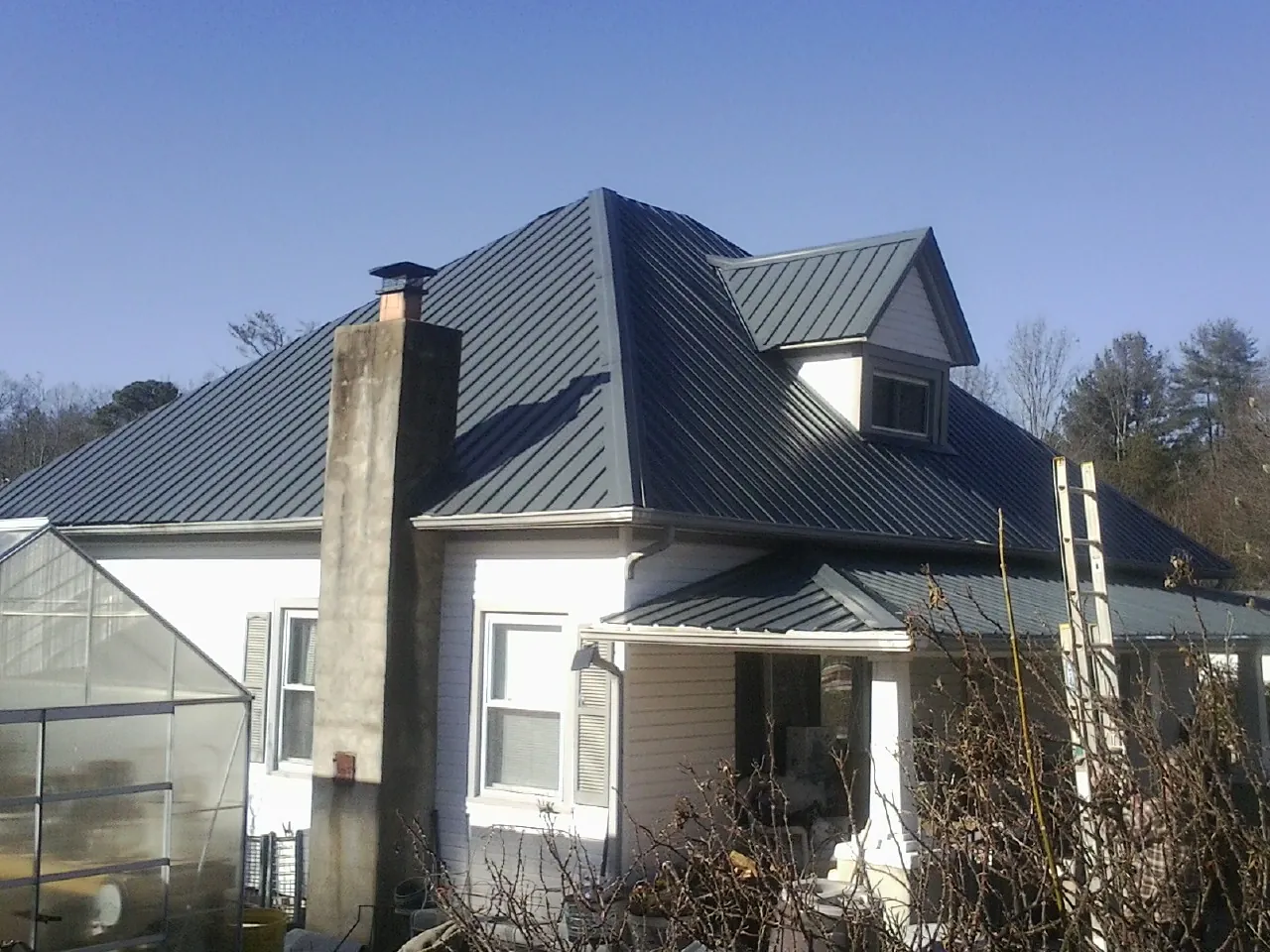 Dark blue standing seam metal roof on a white farmhouse with dormer — Slate & Tile Roof Repair by Roofing Brothers in San Angelo