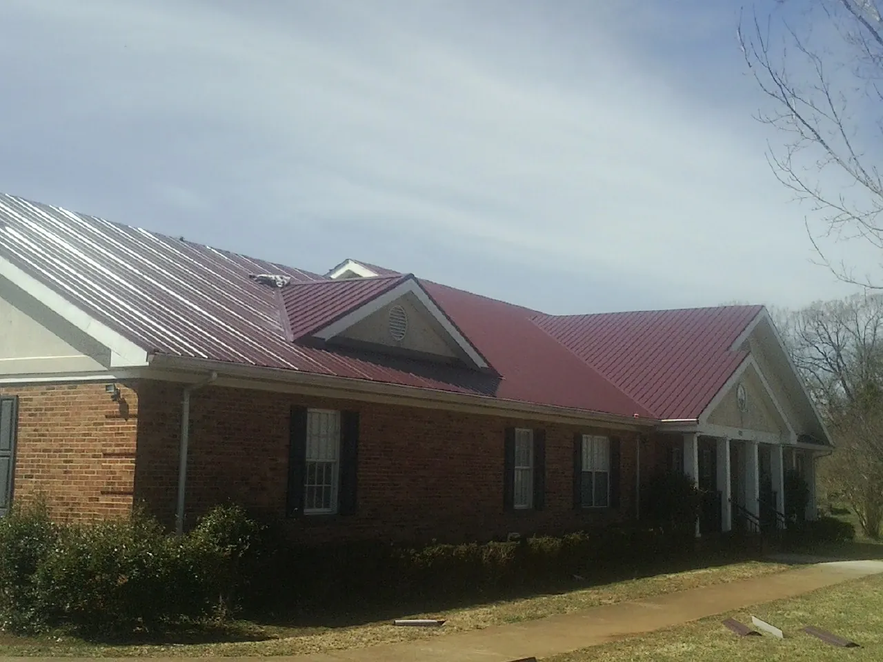 Red metal roof with gabled entries on a long brick building, from a Hail Damage Roof Repair job in San Angelo