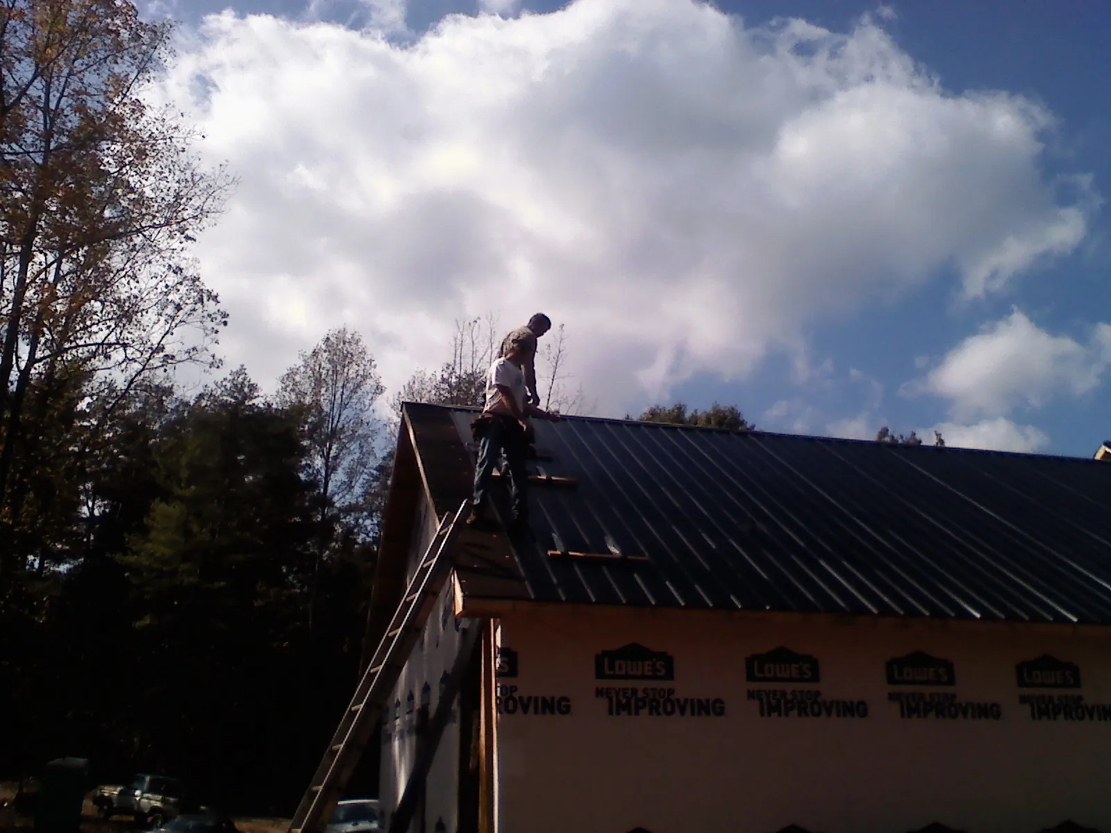Roofer fastening dark metal panels high against a cloudy sky, from a Roof Inspection job in San Angelo