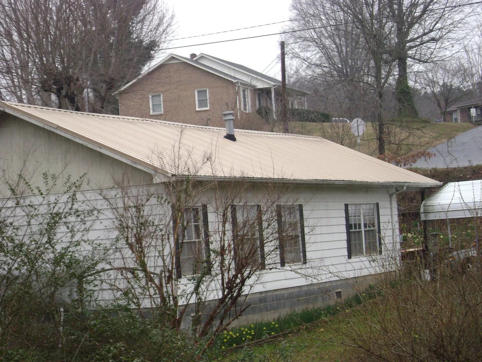 Tan metal roof on a white sided house set into a hillside — Commercial Roofing by Roofing Brothers in San Angelo
